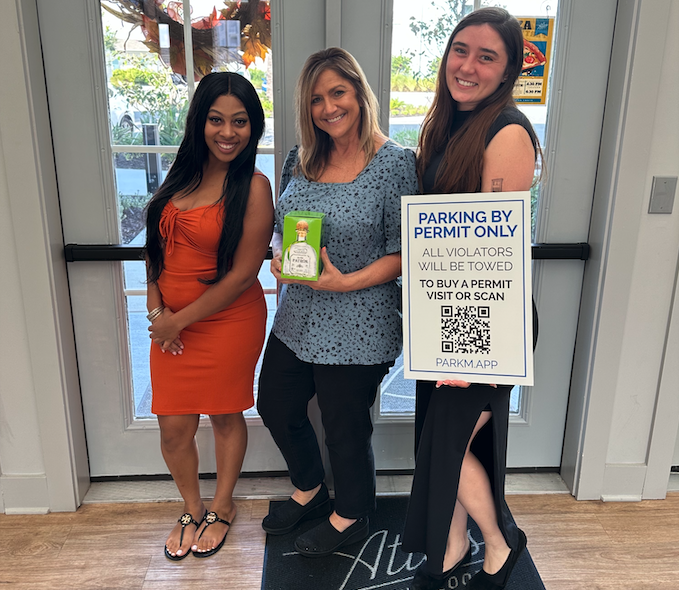 Three property managers holding up a Parkm parking sign in a leasing office