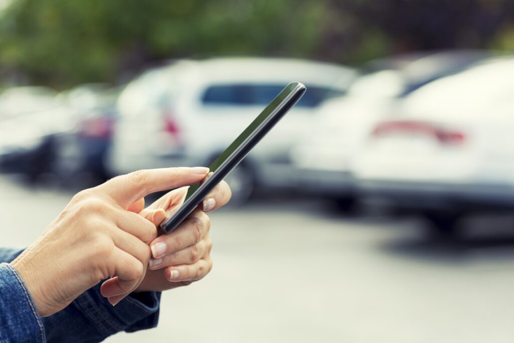 A person accessing a parking app using their cellphone in a parking lot