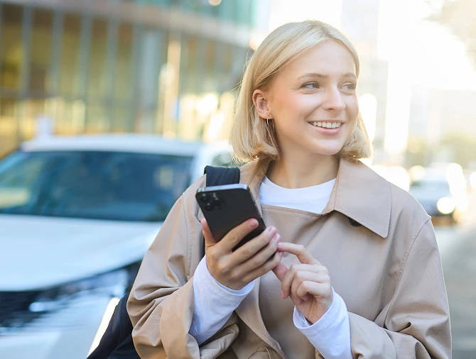 Smiling resident using her phone on the street beside a parked car