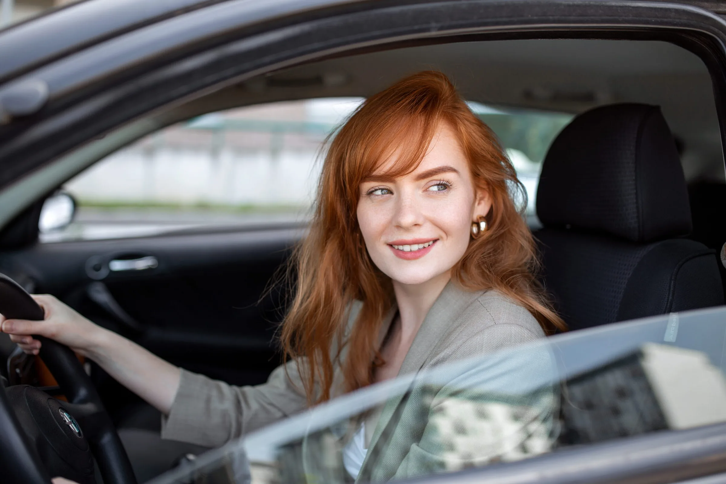Smiling woman at the wheel of her car, looking out the driver's side window