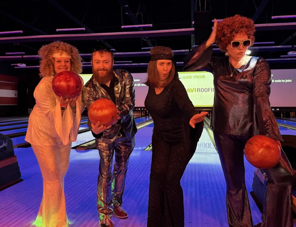 Four ParkM team members in 1970s disco costumes holding bowling balls at a bowling event