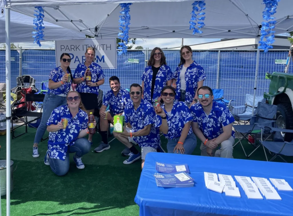 ParkM team in matching blue Hawaiian shirts under a Park It With ParkM tailgate tent
