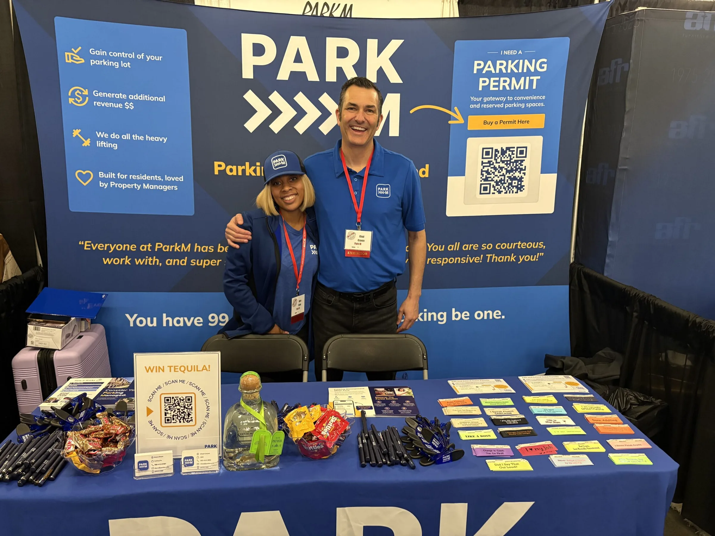 Two ParkM team members at the ParkM trade show booth beside a Buy a Permit Here QR code sign