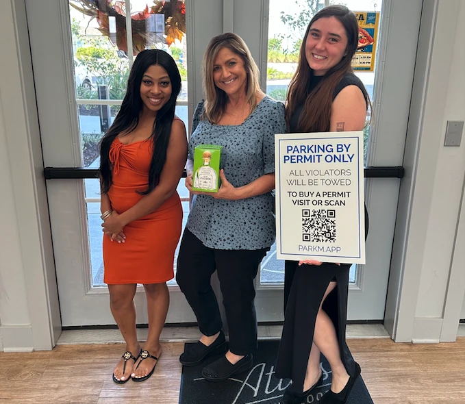 Three property managers holding up a Parkm parking sign in a leasing office